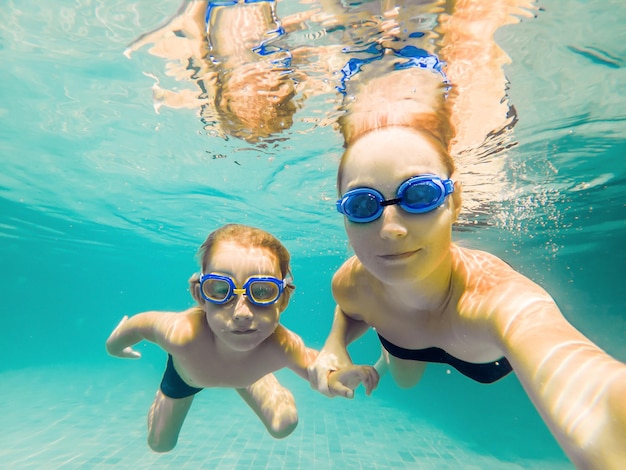 Mom and son in diving glasses swim in the pool under the water