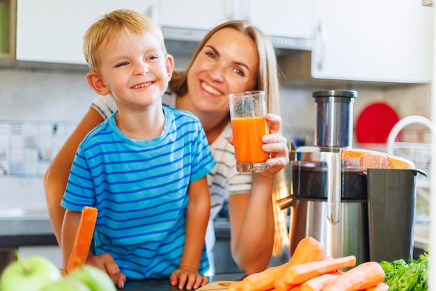 Mom and son drink fresh carrot juice squeezed using juicer in kitchen at home