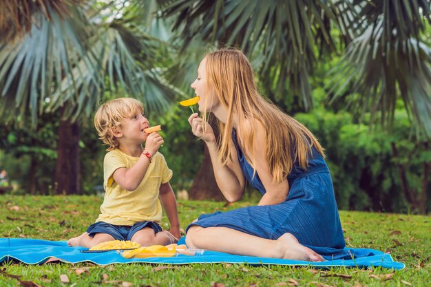 Mom and son had a picnic in the park. Eat healthy fruits - mango, pineapple and melon. Children eat healthy food.