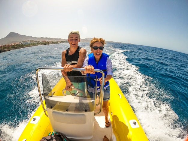 Mom and son having fun and enjoying together in a boat drivig it and discovering the sea smiling and laughing - vacations and holiday outdoors in the water with a dinghy