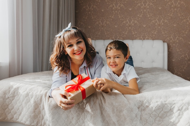 Mom and son lie on the bed. child gives his mom a gift for mother's day.