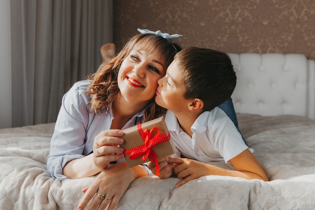 Mom and son lie on the bed. child gives his mom a gift for mother's day.