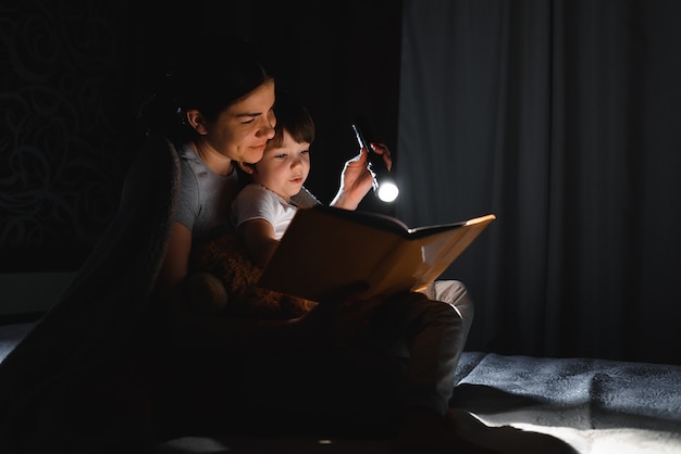 Mamma e figlio che leggono un libro con una torcia sotto la coperta