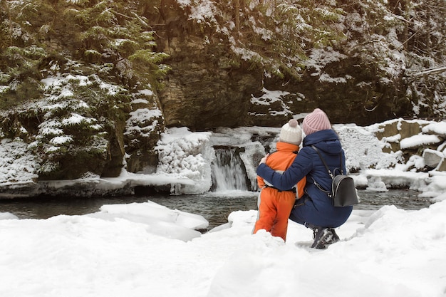 ママと息子の雪の背景に抱擁で座っています。