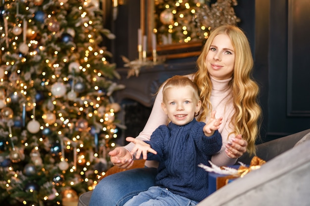 Mamma e figlio che si siedono nella posa di un albero di natale, concetto di festa.