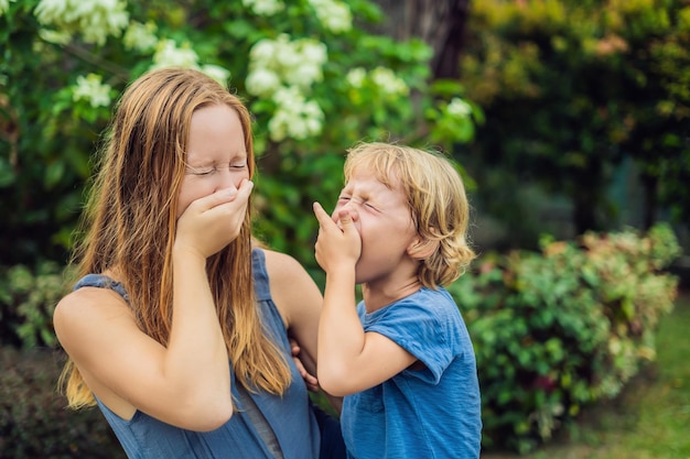 Mom and son sneeze in the park against the background of a flowering tree. Allergy to pollen concept