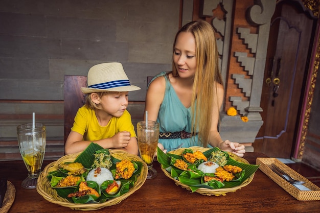 Mom and son tourists in Indonesian food cafe Traveling with kids concept What to do with children Child friendly place