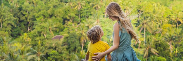 子供と一緒に旅行するジャングルの上の石の上のママと息子の観光客は子供をどうするかを概念化します