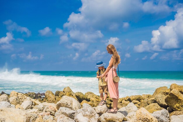 Foto viaggiatori di mamma e figlio sull'incredibile spiaggia di melasti con acqua turchese isola di bali indonesia viaggiare con il concetto di bambini