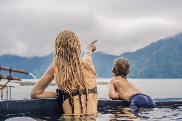 湖を背景にバリの温泉でママと息子の旅行者子供と一緒に旅行のコンセプト