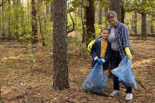 Photo mom and son volunteers with garbage bags collecting plastic waste around the park ecoactivists