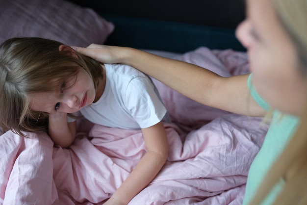 Mom strokes a frustrated little girl on the bed at home