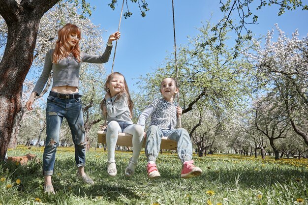 Photo mom swings her little daughters on the garden swing