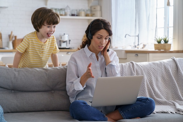 子供の子供たちと一緒に自宅からラップトップでビデオ通話のリモートワークで話しているお母さんは、舌を鳴らします