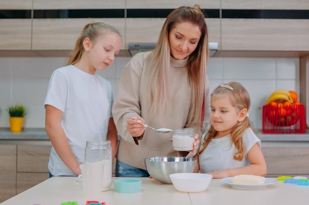 La mamma insegna alle sue figlie a cucinare la pasta in cucina.