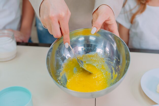 Mom teaches her daughters to make dough in the kitchen and beat\
eggs.