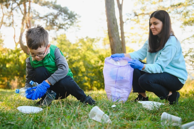 Mom teaches her son to clean up trash in nature. A woman removes plastic bottles in a bag. The topic of environmental pollution by garbage.