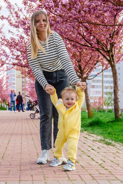 mom teaches her son to walk holding his hands in a park with cherry blossoms