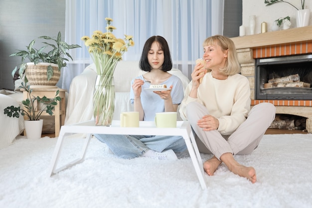 Mom and teenage daughter eating dessert in living room at home, Happy family together.