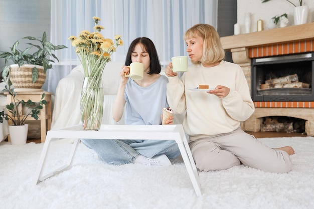 Mamma e figlia adolescente che mangiano dessert nel soggiorno di casa, famiglia felice insieme.