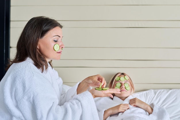 Mom and teenage daughter taking care of face using natural cosmetics and cucumber