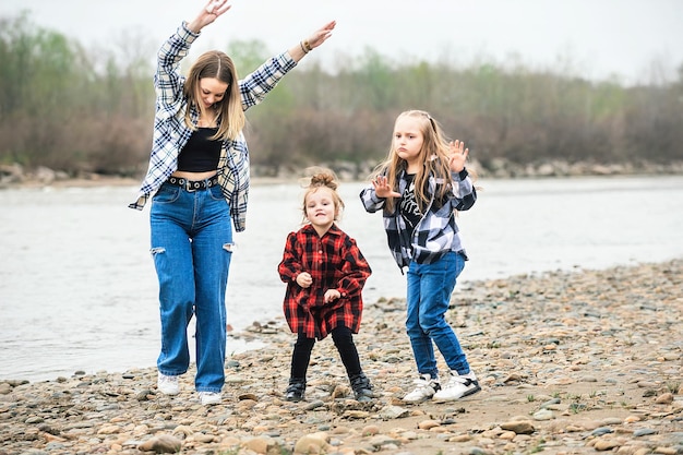 mom together with two daughters have fun and dance on a walk by the river