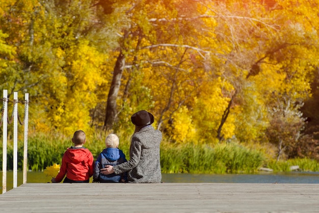 Mom and two children are sitting on the pier. Sunny autumn day. Back view