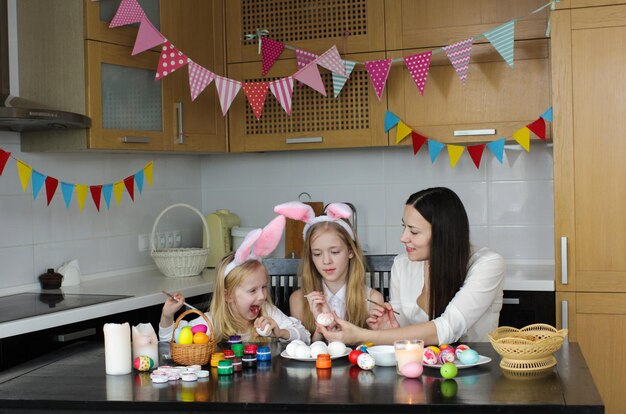 Mom and two little daughters draw Easter eggs. A happy family is preparing for Easter.