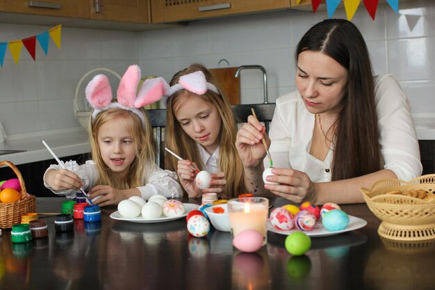 Mom and two little daughters draw Easter eggs. A happy family is preparing for Easter.