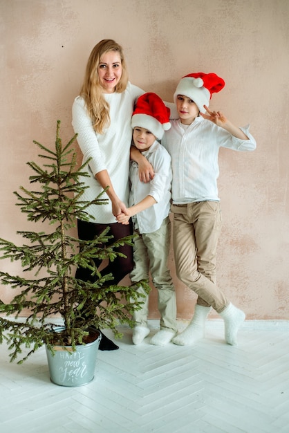 분홍색 벽과 크리스마스 트리 옆에 엄마와 두 아들. 미니멀리즘.