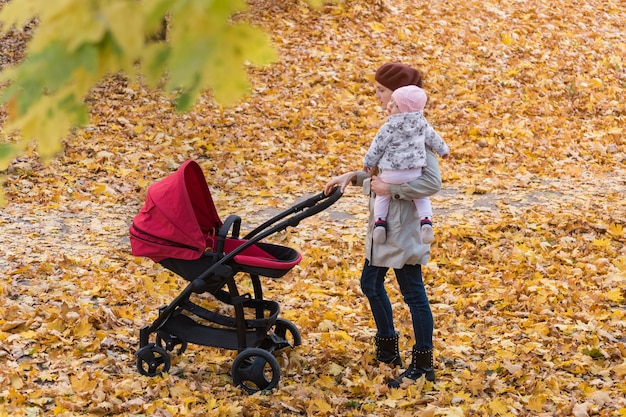 Mom walks in autumn Park with baby Stroller. Mother and child in autumn forest.
