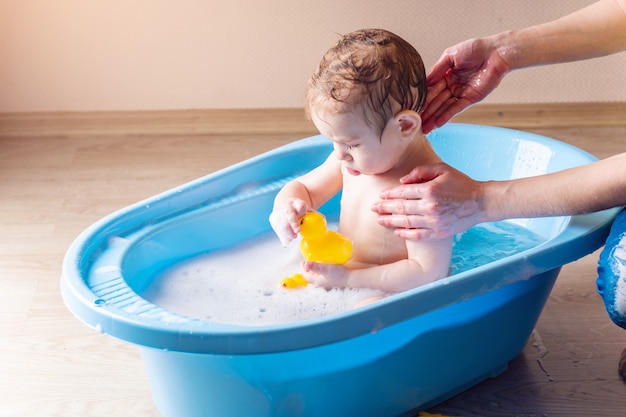 Mom washing little boy in a blue bath in the bathroom. 