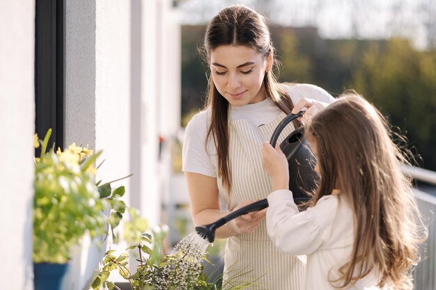 Mom watering plant with her adorable little daughter happy family gardening on balcony