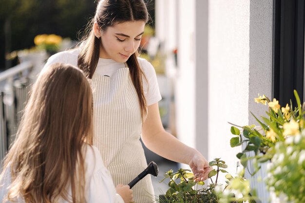 Mom watering plant with her adorable little daughter happy family gardening on balcony