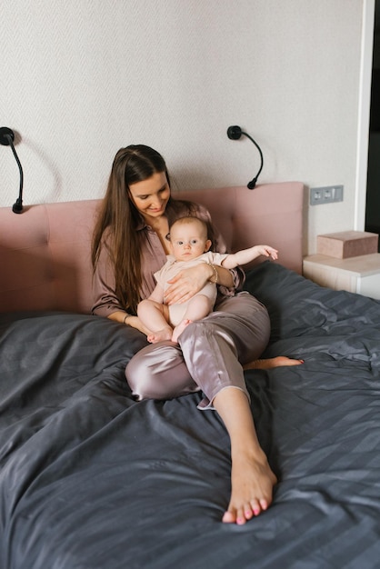 Mom with a baby in her arms sits in the bedroom on the bed