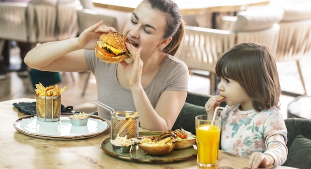 Mom with a cute daughter eating fast food in a cafe