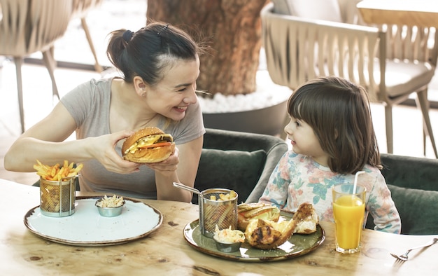 Mom with a cute daughter eating fast food in a cafe