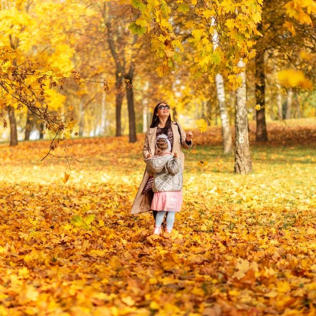 Mom with her baby daughter are walking in the autumn park with golden fall foliage