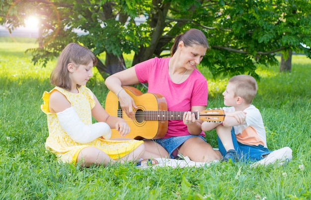 Mom with her two children play guitar at the park.