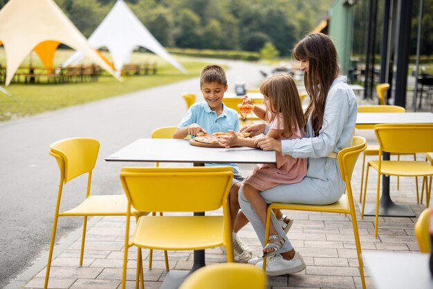 Photo mom with kids eating pizza at amusement park