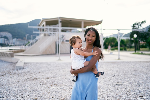 Mom with a little daughter in her arms stands on the beach