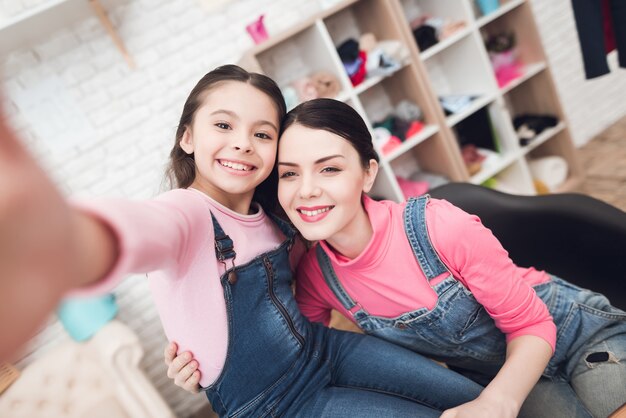 小さな女の子とお母さんは、スマートフォンでselfieをします。