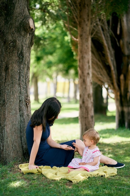 Mom with a little girl sit on a blanket on a green lawn