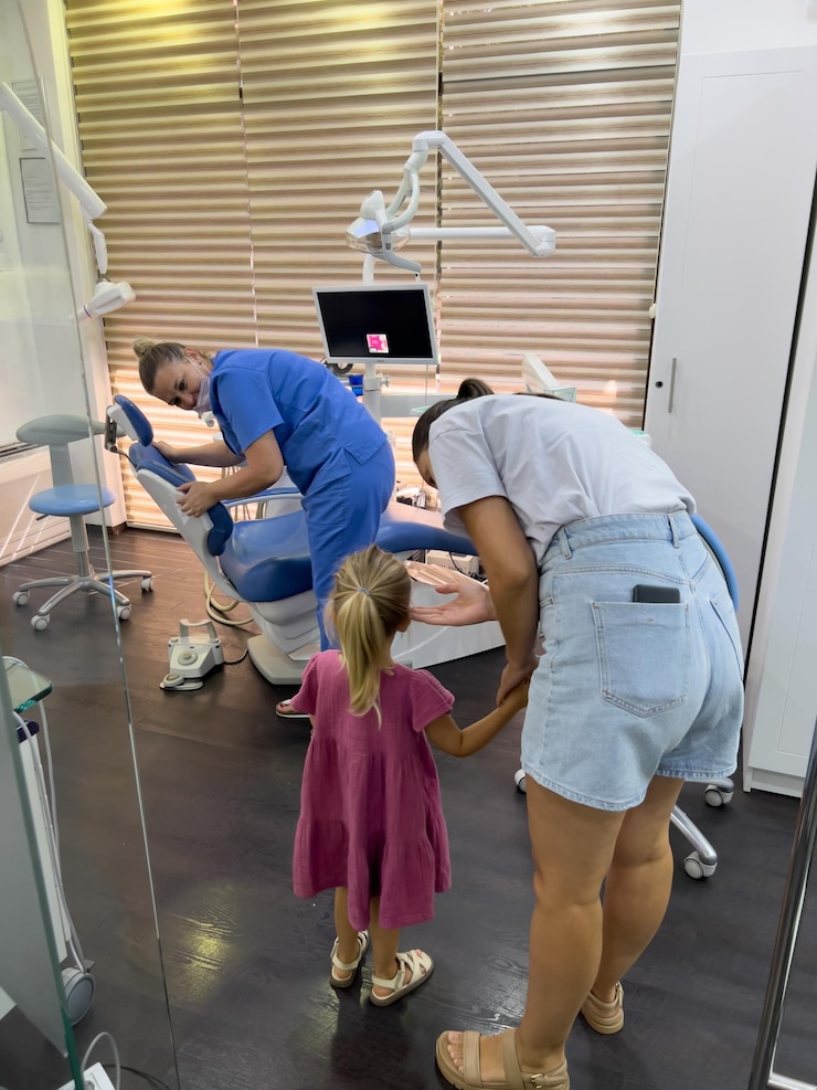 Photo mom with a little girl stand near the dentist adjusting the dental chair