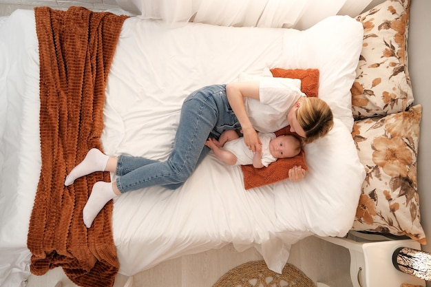 Mom with a newborn baby lies on the bed mother kisses the child mother's love