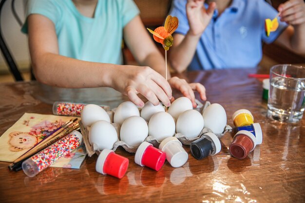 Photo mom with two children decorate easter eggs sitting at the table at home in the kitchen