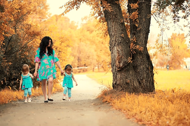 Мама с двумя дочерьми-близнецами на прогулке в осеннем парке
