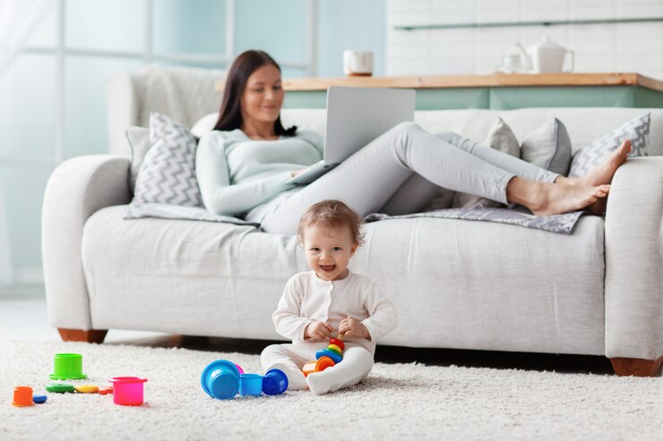 彼女の子供が床におもちゃで遊んでいる間、ママは自宅のラップトップで働いています