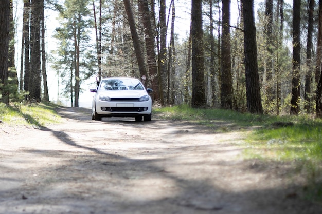 современный автомобиль едет в лесу. белый автомобиль стоит на лесной проселочной дороге летний солнечный день. водитель и пассажир машут руками