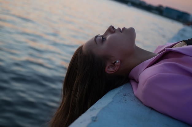 Photo a moment of calm in the urban space, a young woman feels relaxation by laying her head and looking at the sky, lying against the background of the sea